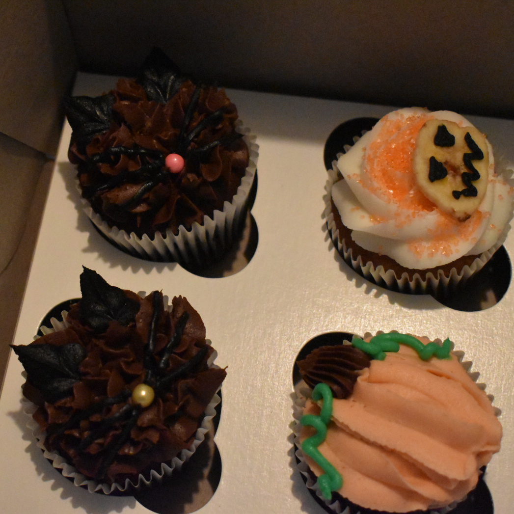 halloween themed cupcakes, two decorated like cats, two as pumpkins