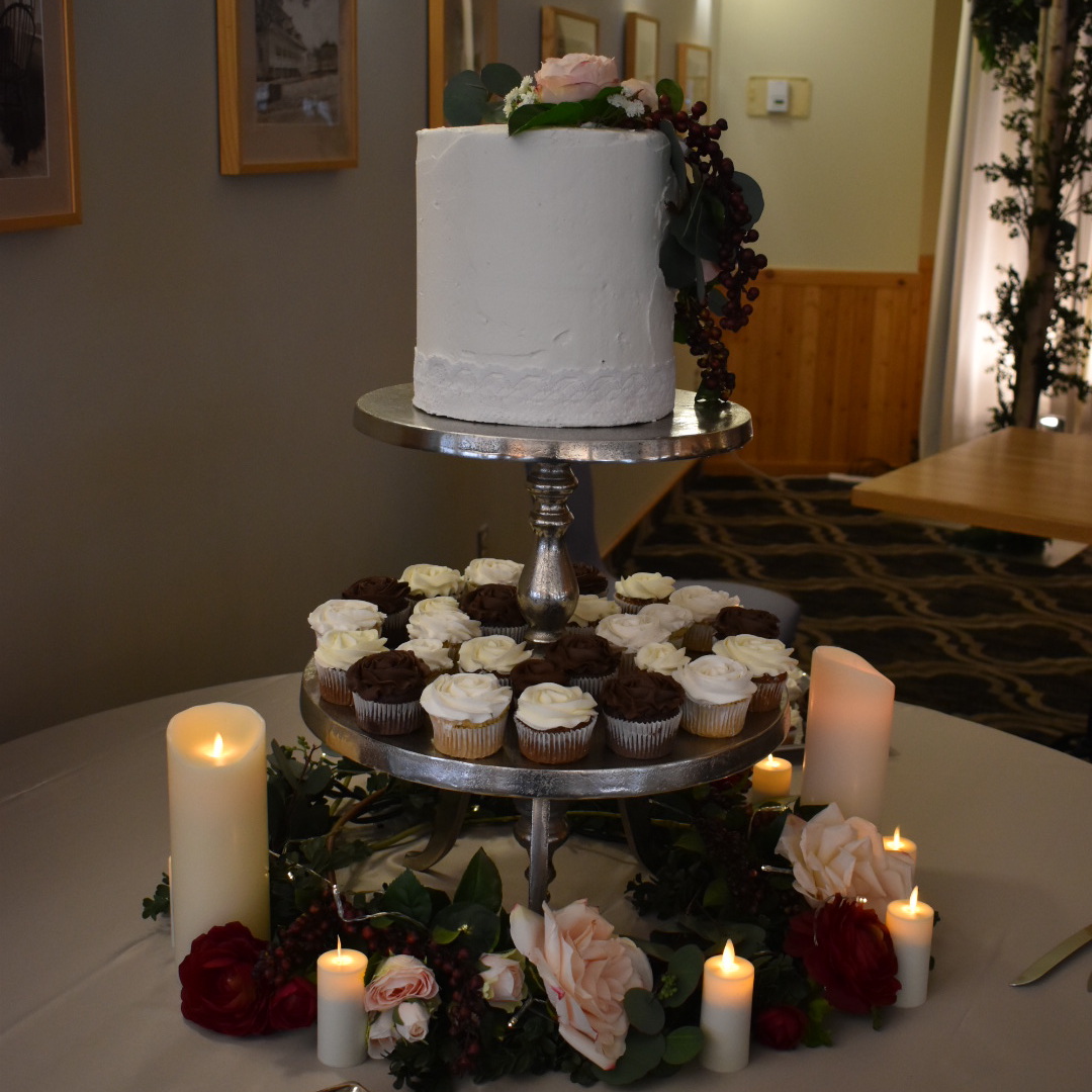 wedding cake with on pedestal surrounded by cupcakes and candles