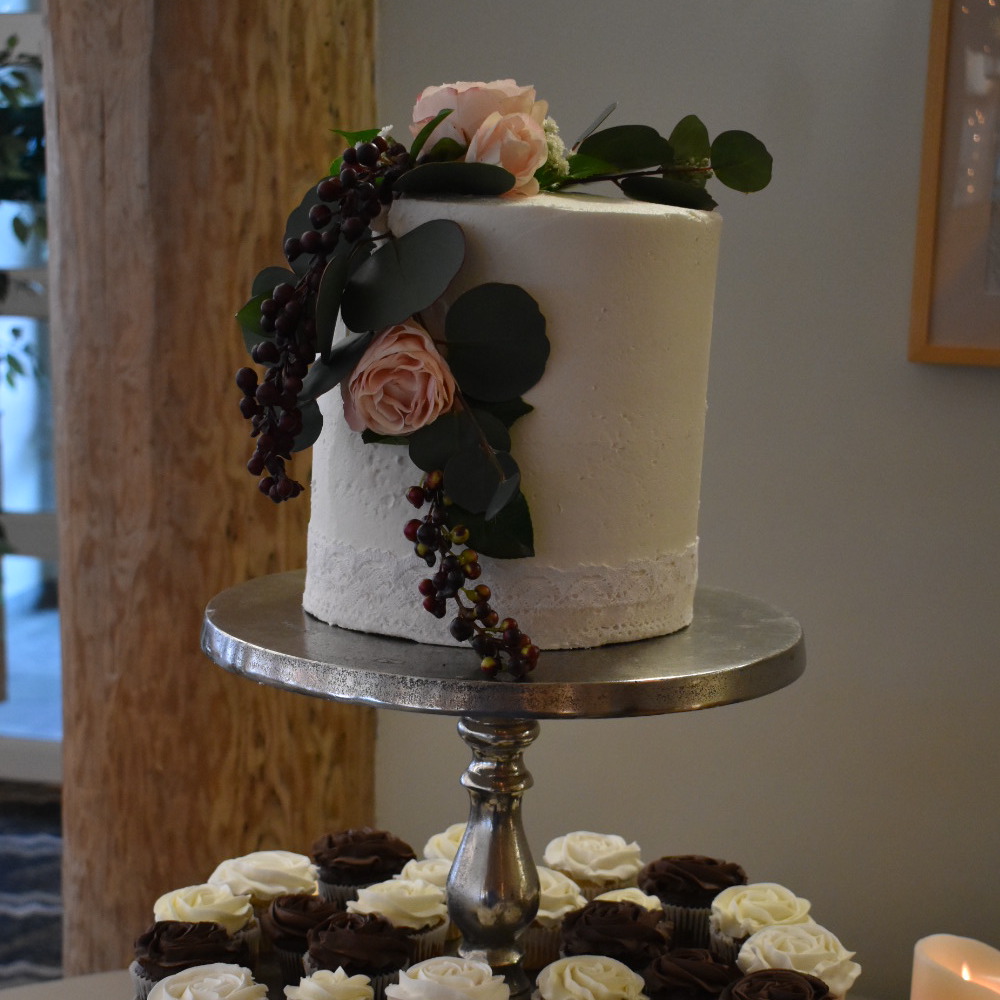 wedding cake on pedestal with flowers flowing down the side